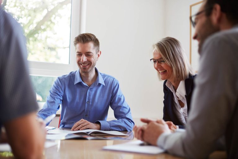 Ein Businessmeeting mit unterschiedlichen Kollegen, die lachen und sich unterhalten.