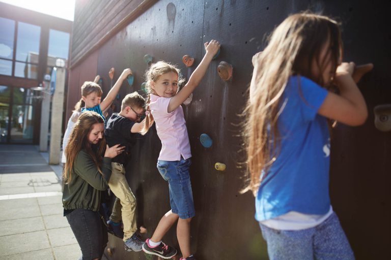 Kinder krettern an einer Kletterwand entlang, ein Mädchen schaut den Betrachter an.