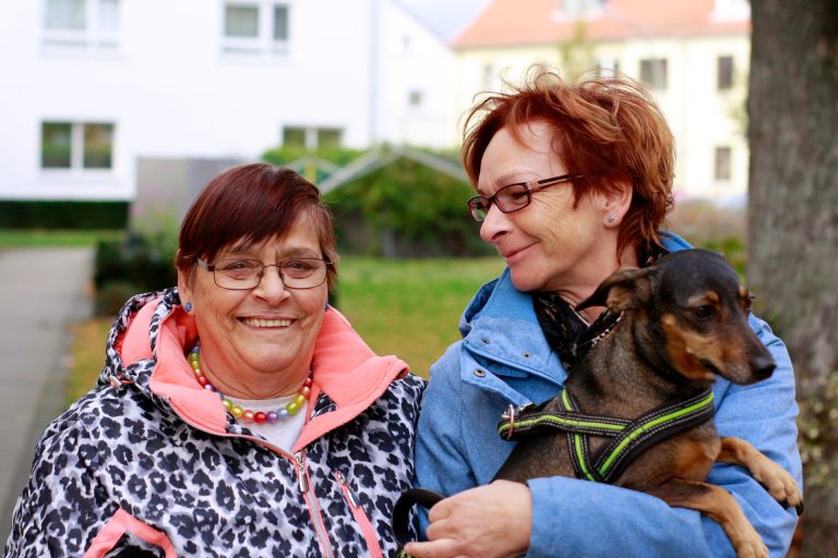 Eine ehrenamtliche Helferin steht neben einer Dame. Sie gehen Gassi.