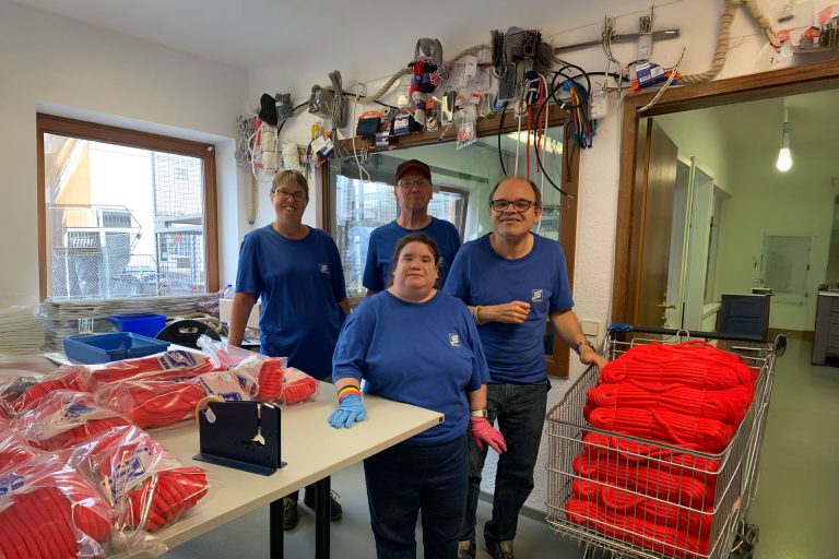 Inklusives Arbeiten bei der Lebenhilfe Braunschweig in Zusammenarbeit mit Seilflechter. Ein Team verschiedener Menschen in einer Werkstatt schaut glücklich in die Kamera.